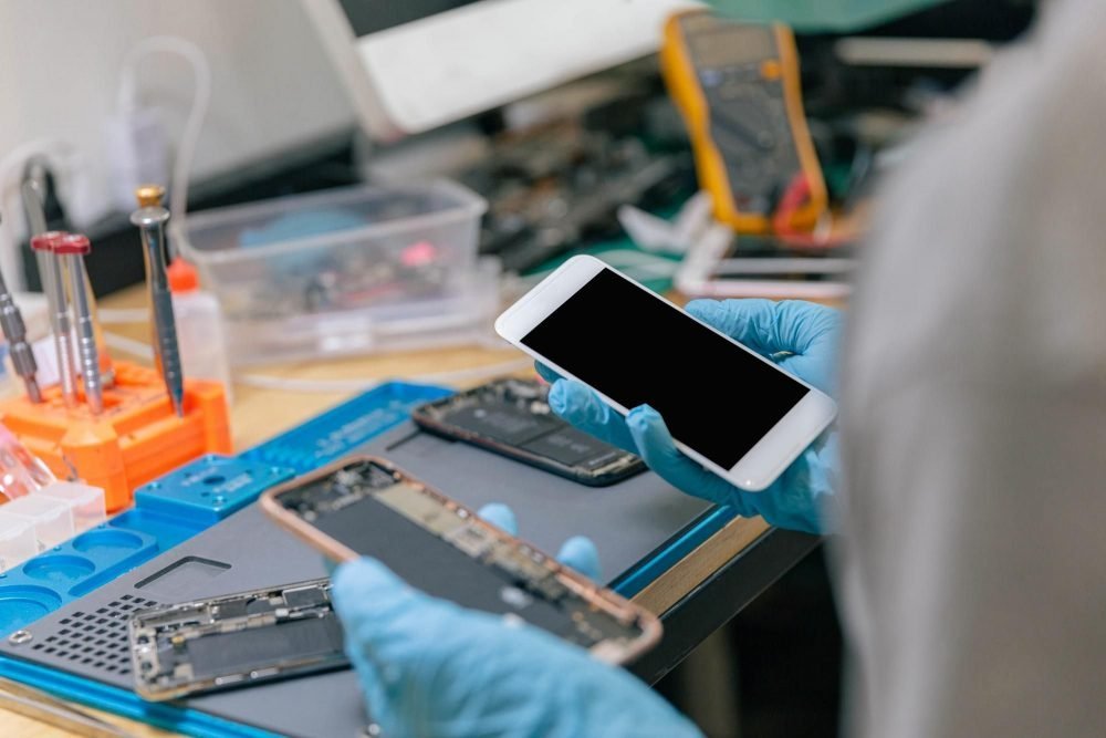 Manos con guantes azules sostienen un celular abierto en una mesa de reparación